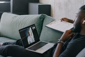 In this image a guy is sitting which his laptop, doing online meeting